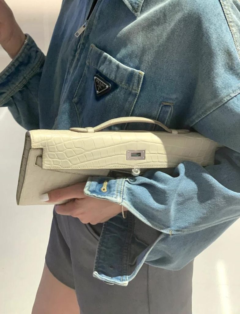 Woman holding a Hermès Kelly Cut clutch in white crocodile leather