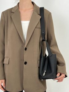 A stylish black Picotin Hermes bag carried by a woman in a brown blazer.