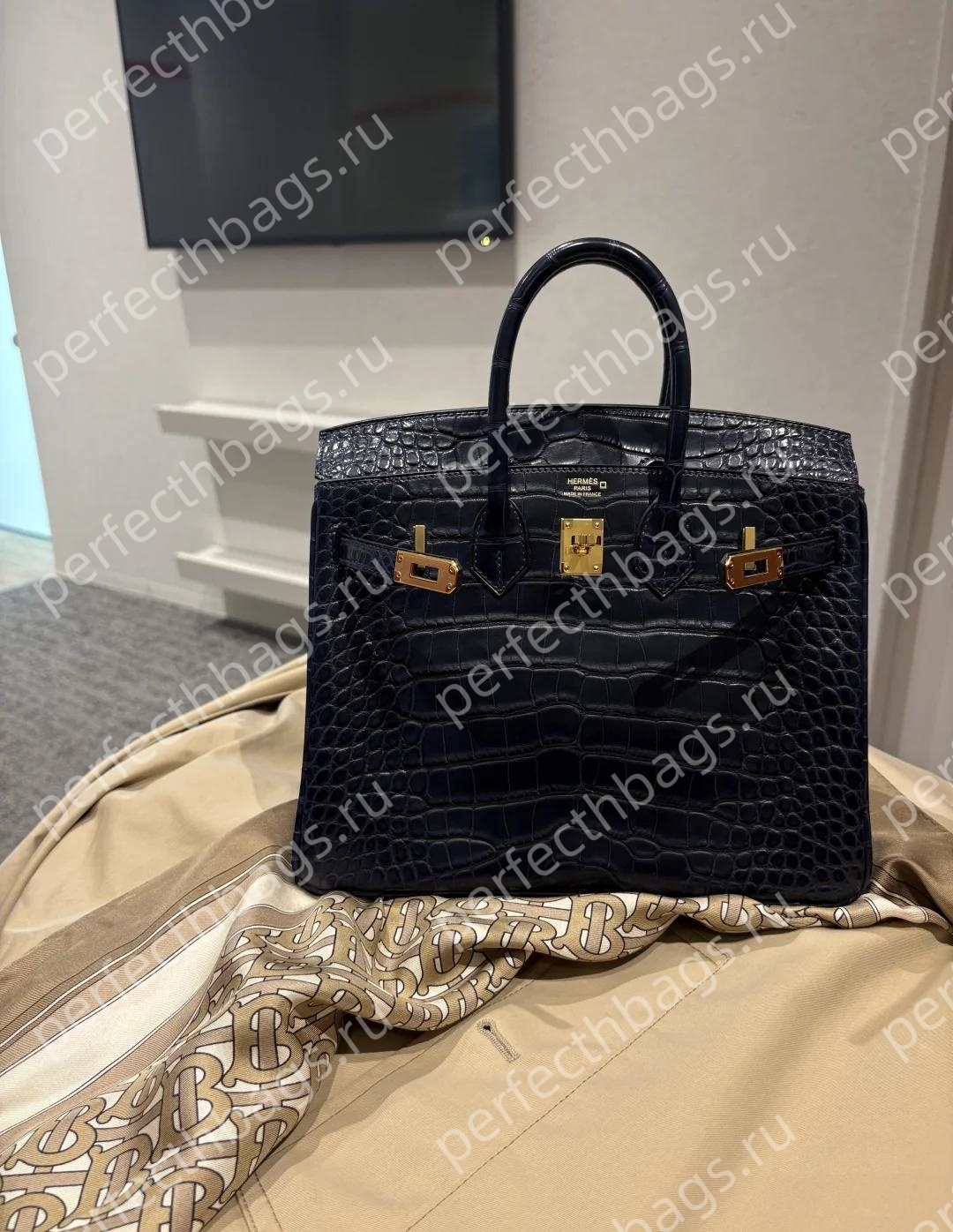Navy blue crocodile skin Birkin bag with gold hardware displayed on a luxury coat, exotic skin texture details.